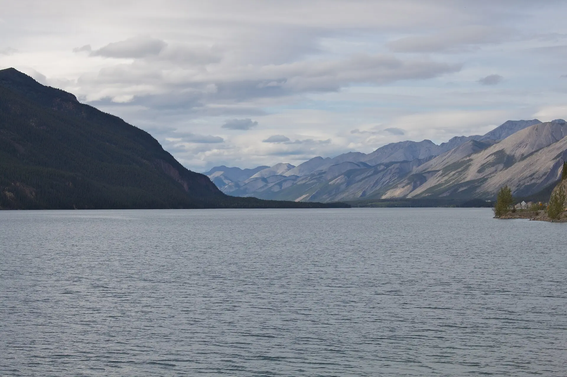 Jade-green Muncho Lake with forested mountains reflected in calm water along the Alaska Highway