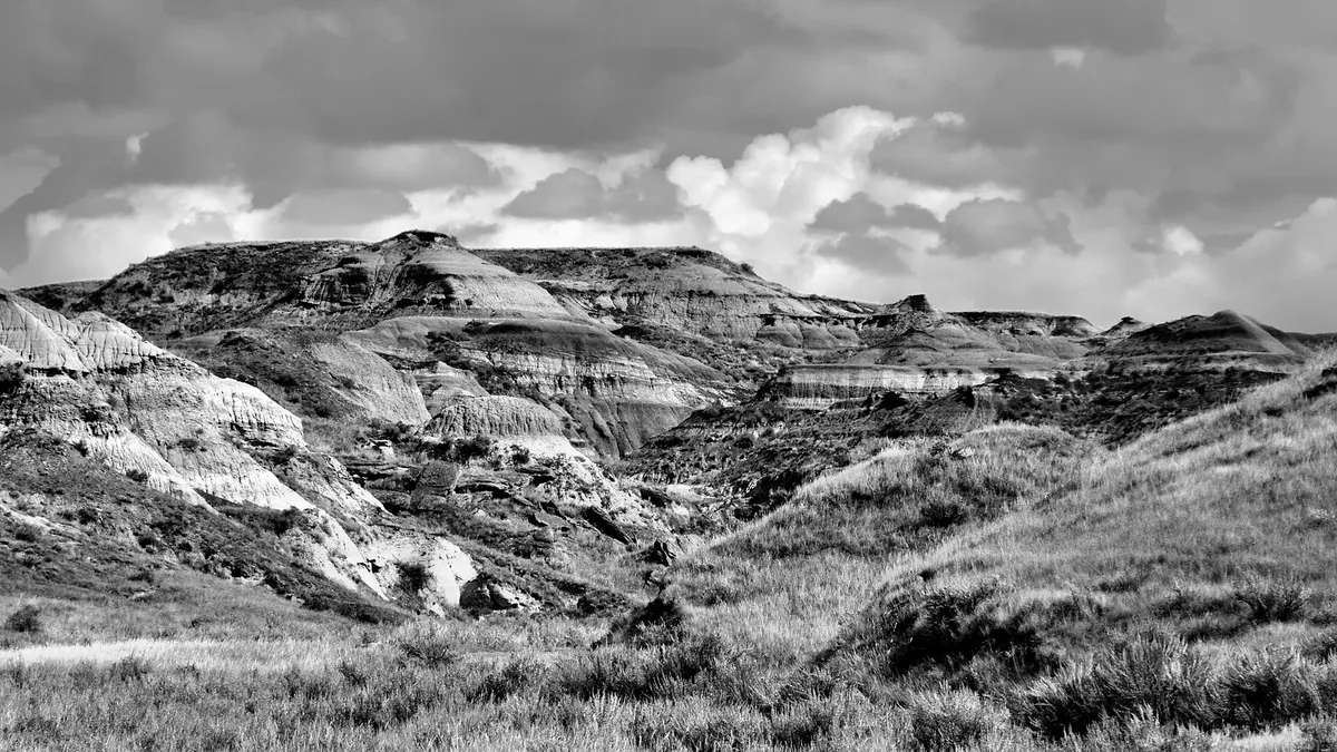 Layered grey and ochre badland ridges in the Red Deer River valley at Dinosaur Provincial Park under a blue sky