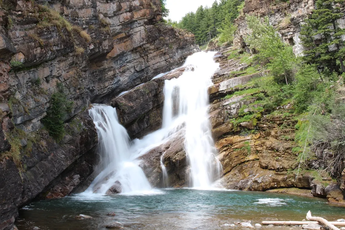 Cameron Falls tumbling over dark layered rock ledges in the middle of Waterton townsite, framed by green trees