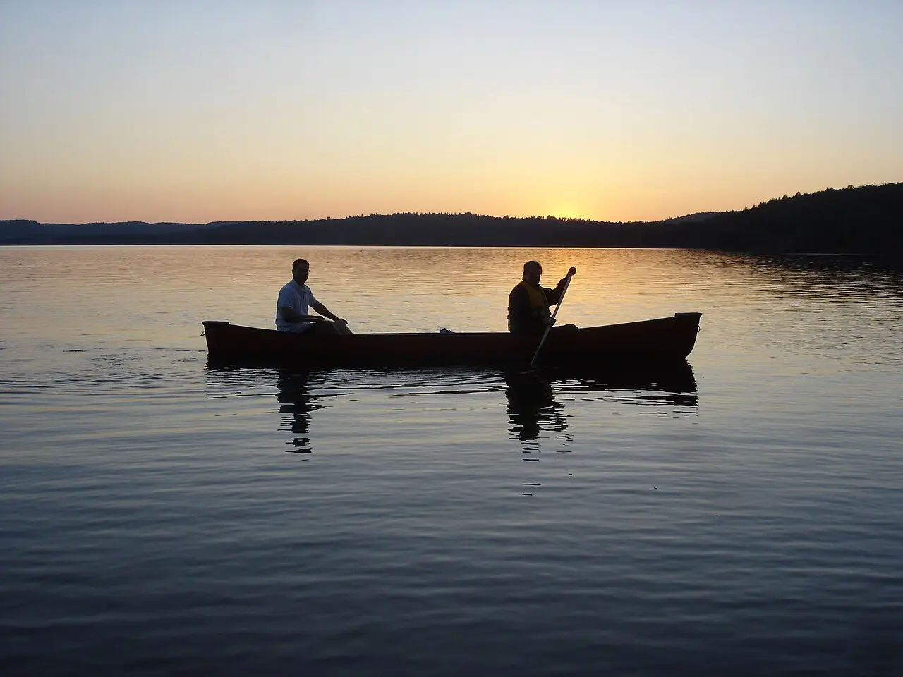 Canoeists paddling a calm lake framed by forest in Algonquin Park