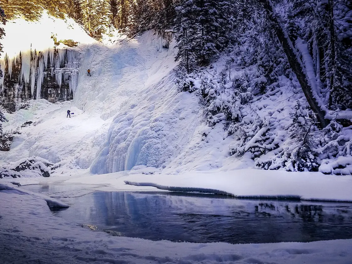Two ice climbers on a frozen waterfall in Johnston Canyon, roped and swinging axes into blue ice