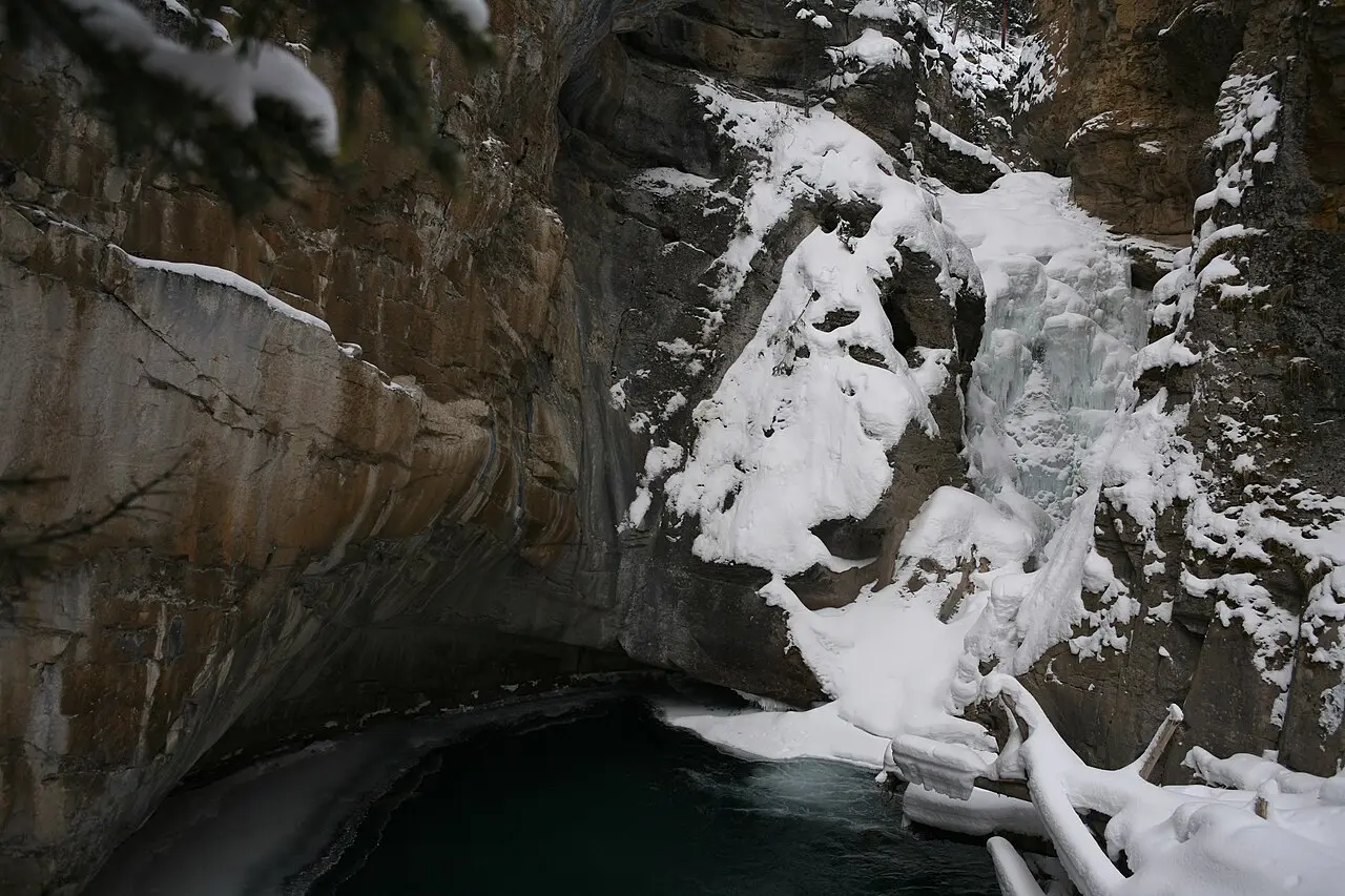 The Lower Falls at Johnston Canyon frozen into thick blue and white ice between dark rock walls