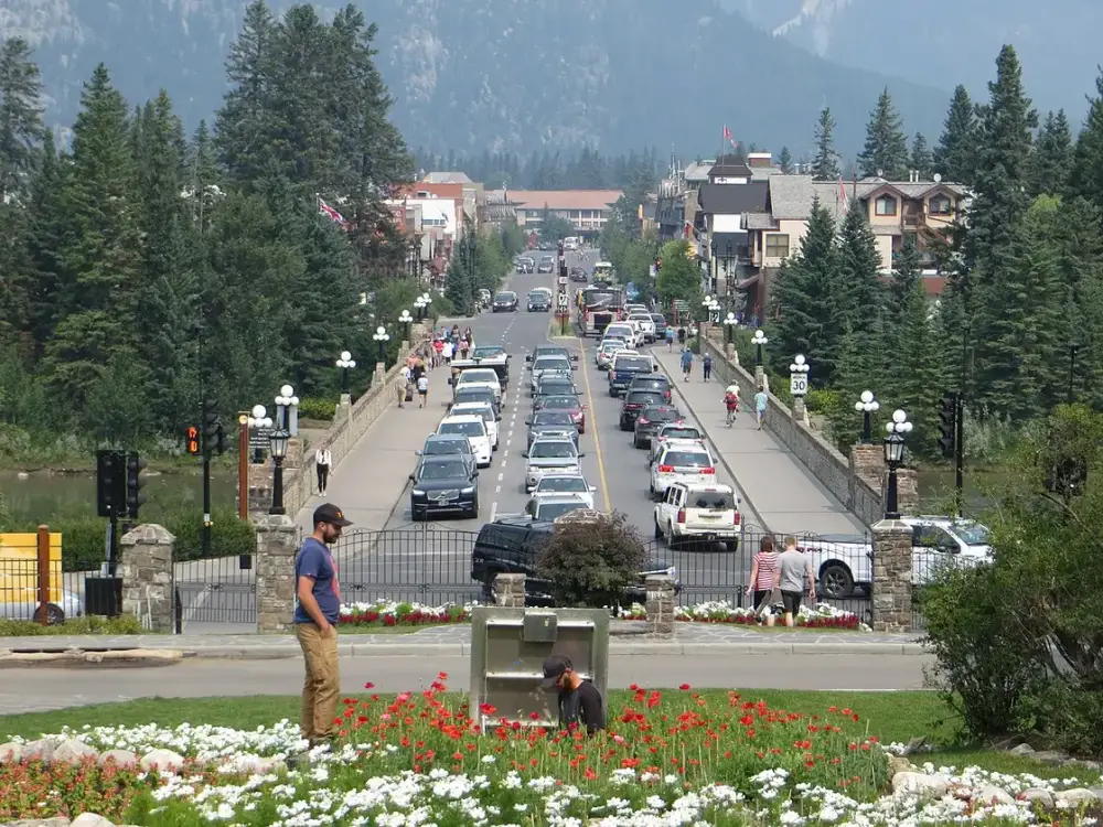 Banff Avenue looking north from the Bow River bridge, lined with shops and cars, with forested mountains behind