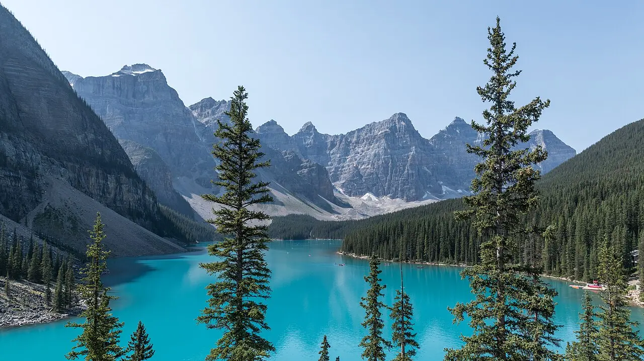 Turquoise water of Moraine Lake below the bare grey peaks of the Valley of the Ten Peaks, framed by spruce trees