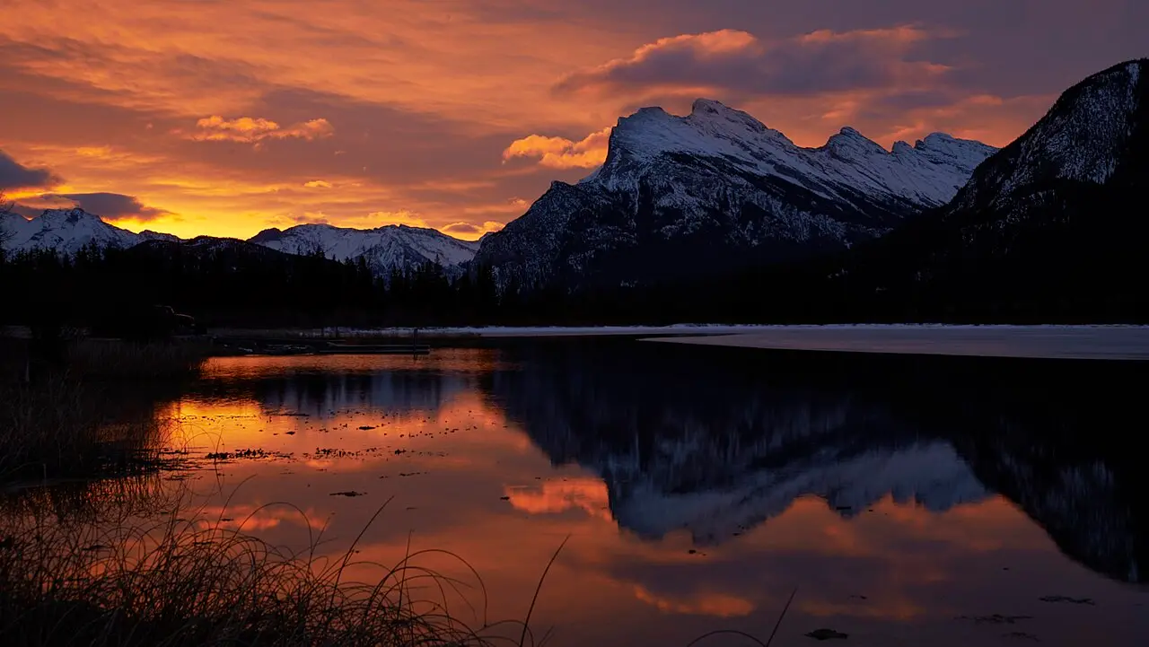 Sunrise over Vermilion Lakes with orange clouds and the snow-covered ridge of Mount Rundle mirrored in still water