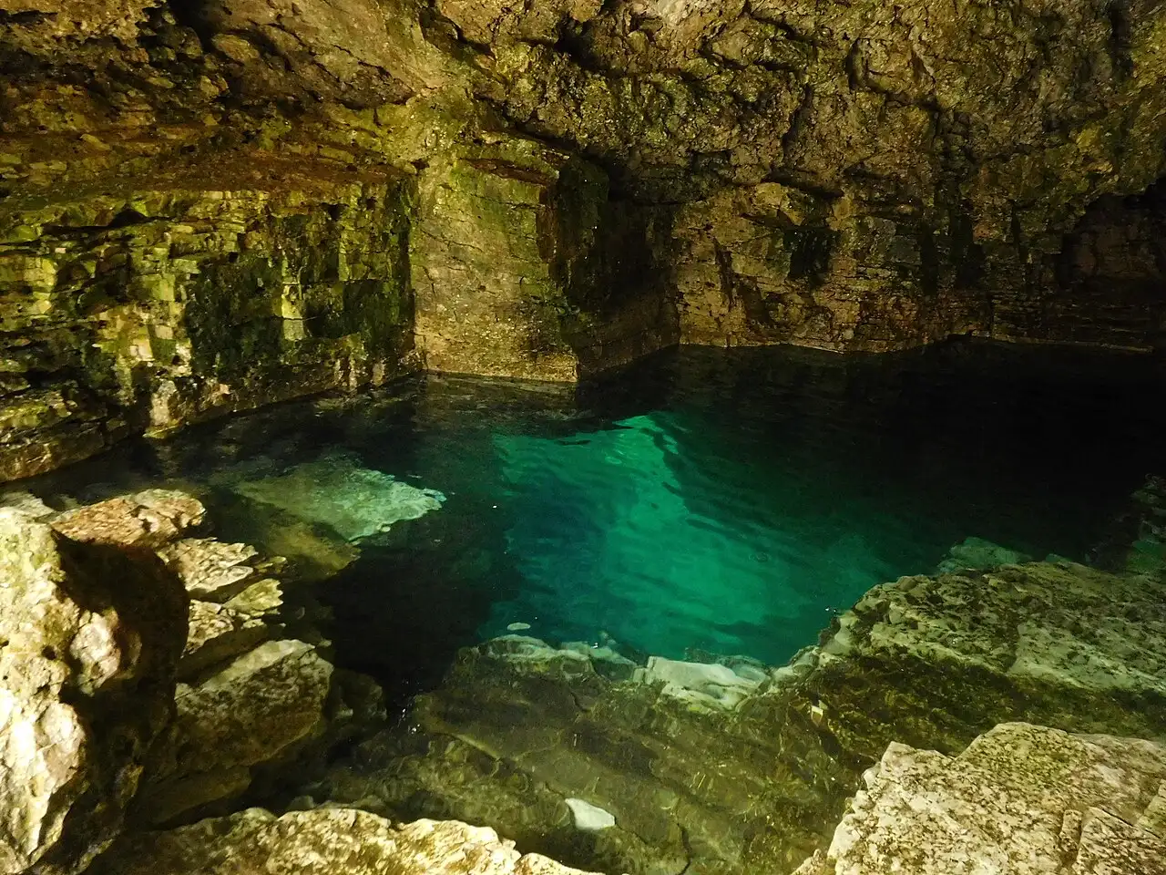 People at the Grotto swimming hole with turquoise water under limestone walls