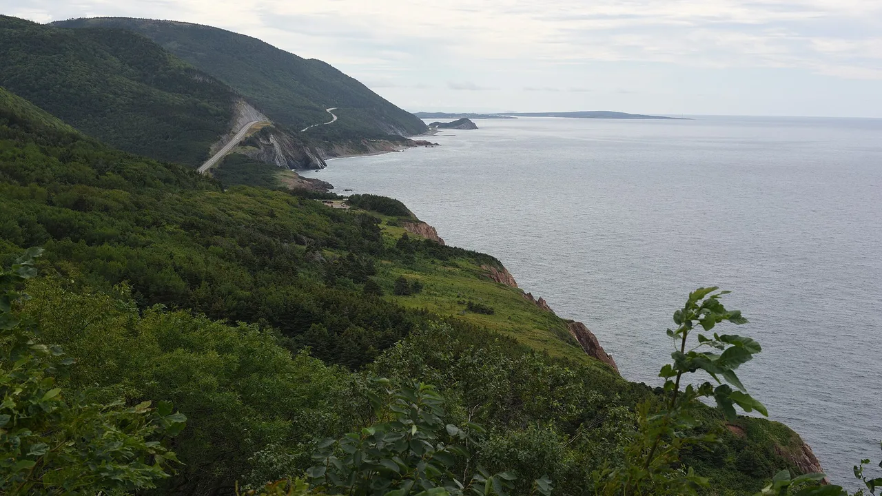 The Cabot Trail curving along a steep green mountainside high above the ocean on the west coast of Cape Breton