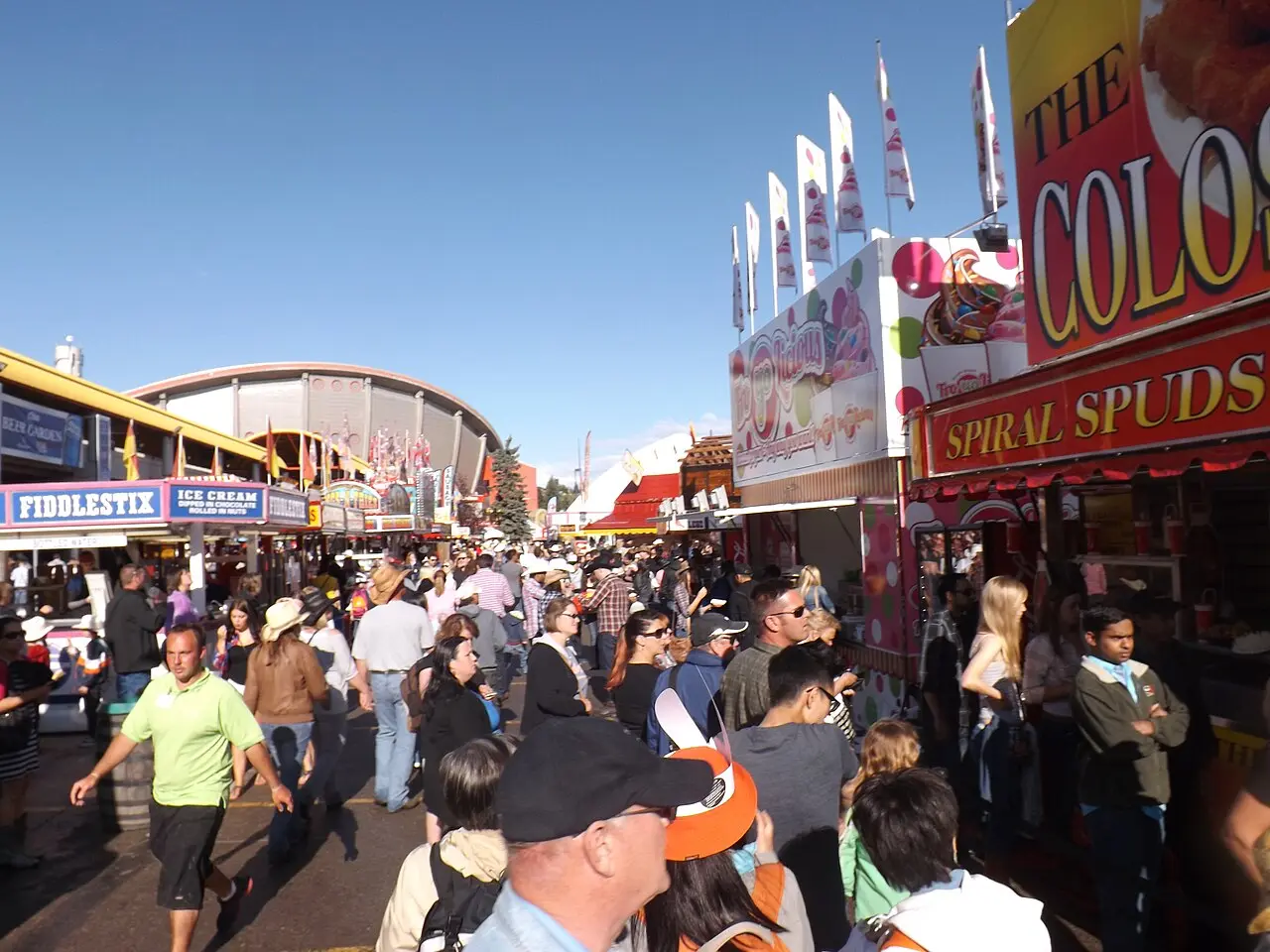 Crowds walking between Stampede fairground stalls and rides under summer daylight