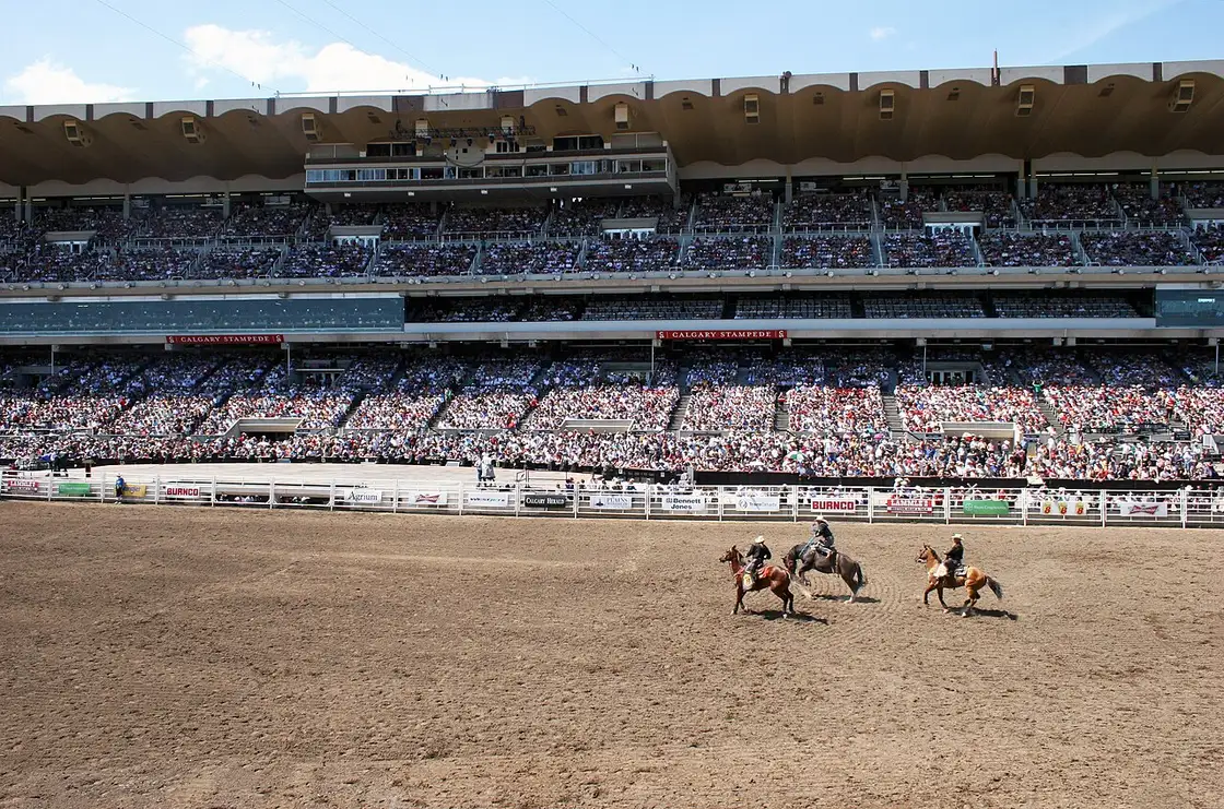 Rodeo action in the dirt arena at Stampede Park with riders and horses under a bright sky