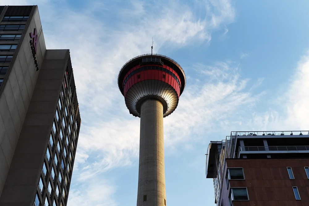 The Calgary Tower seen from street level between two buildings, its red-banded observation pod against a blue sky