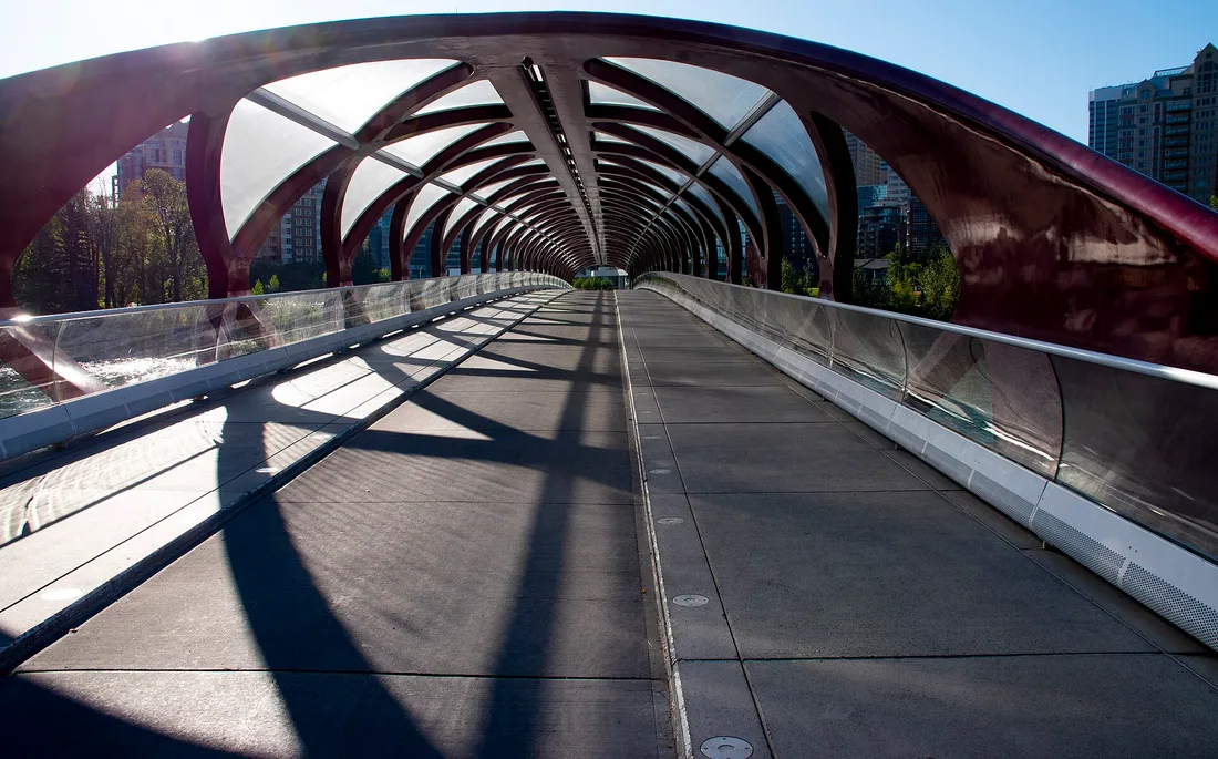 Looking along the inside of the Peace Bridge in Calgary, a tunnel of red steel helix ribs with glass panels