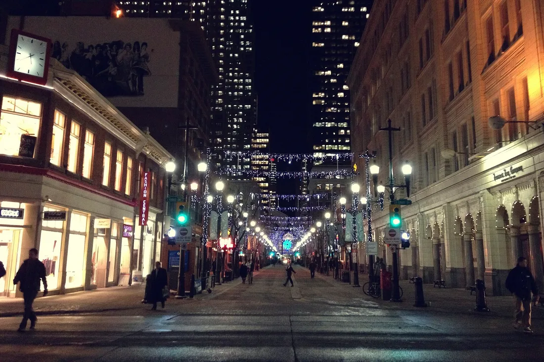 Stephen Avenue in Calgary on a December evening, wet pavement reflecting shop lights and strings of bulbs overhead