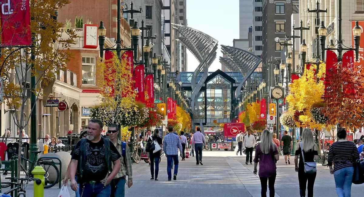 Pedestrians walking down Stephen Avenue in downtown Calgary between historic facades and autumn trees hung with red banners