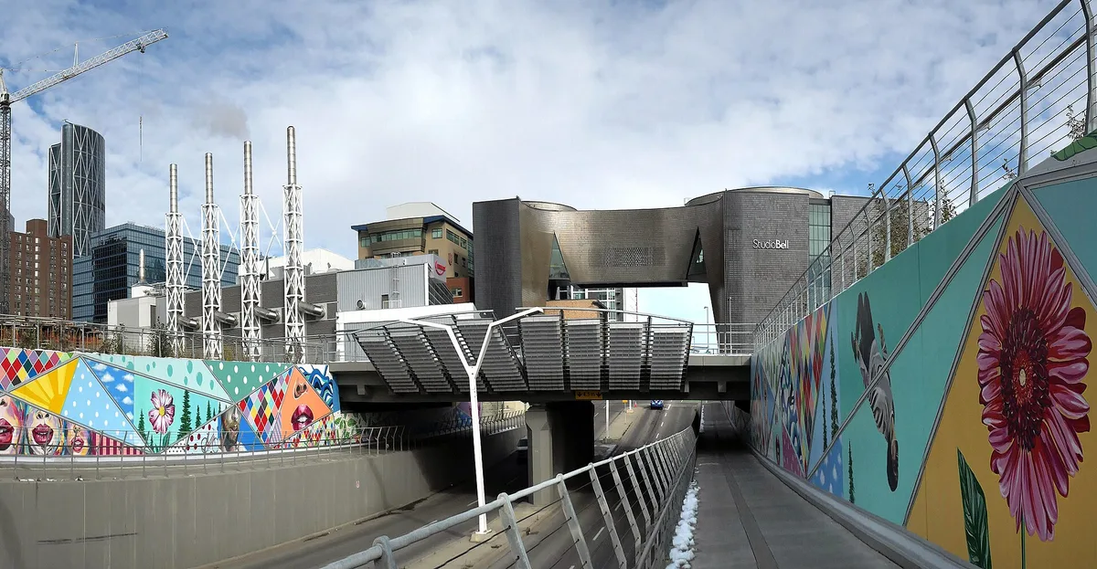 The curved terracotta-clad blocks of Studio Bell in Calgary East Village, with painted murals lining the underpass in front