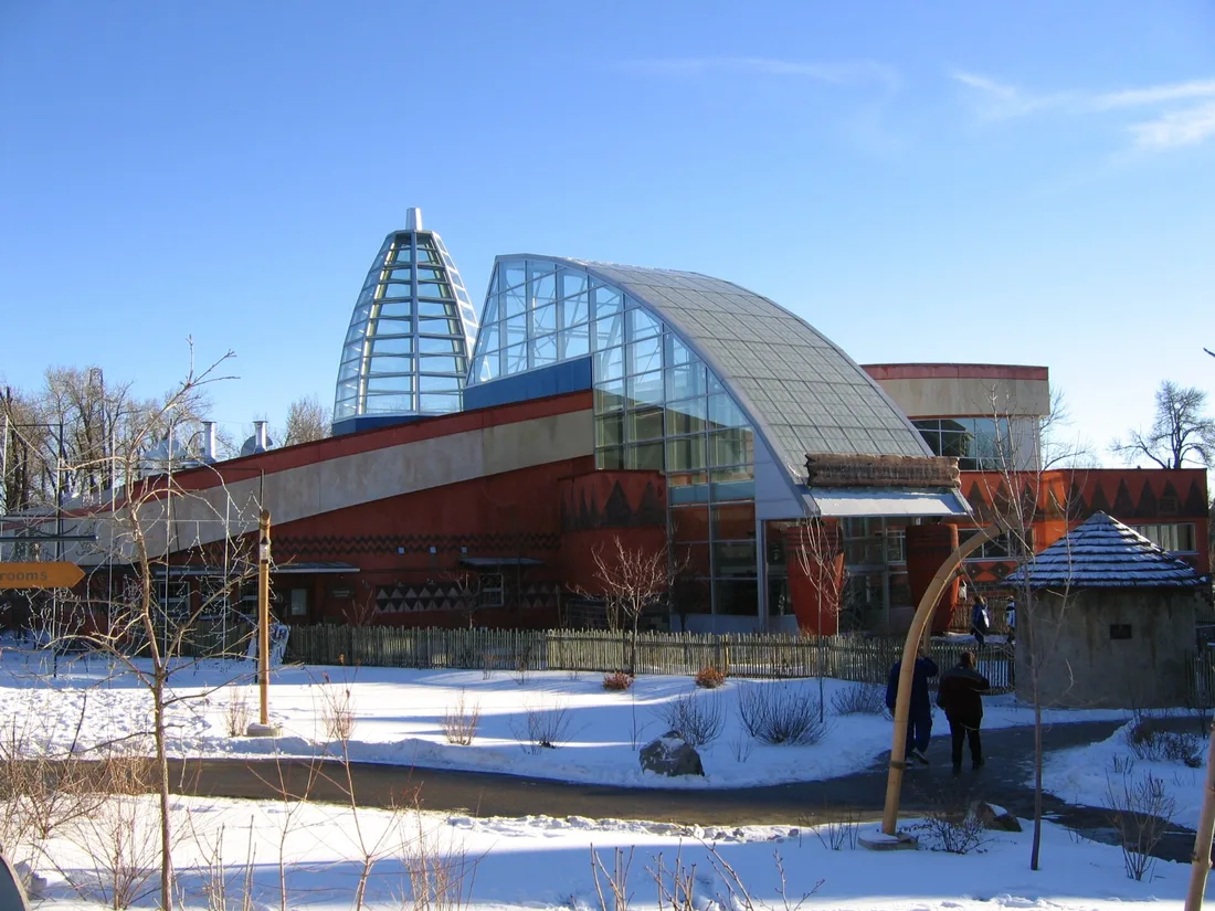 The curved glass and red-ochre pavilion of the Africa building at the Calgary Zoo on a clear winter day with snow on the ground