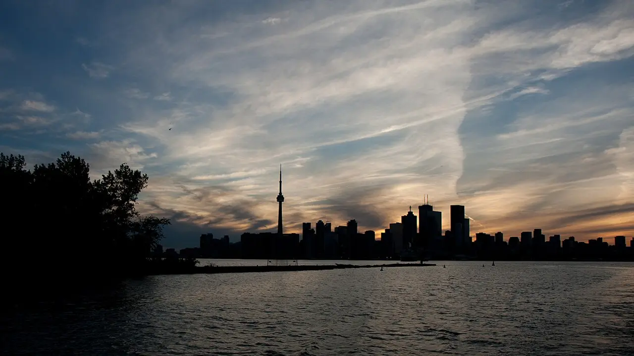 The Toronto skyline and the CN Tower silhouetted against an orange sunset over Lake Ontario