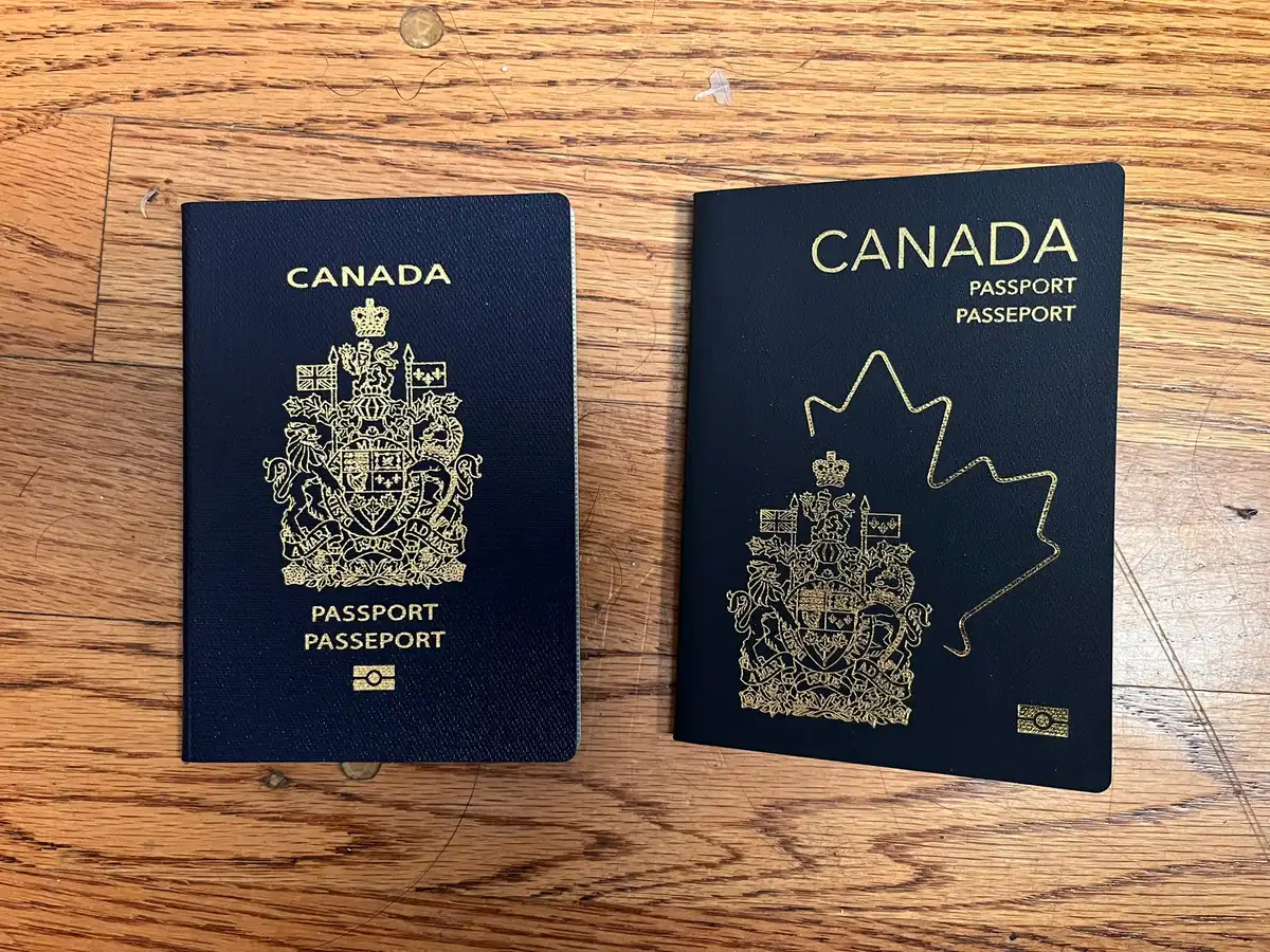 An older blue Canadian passport and a newer version laid side by side on a wooden surface