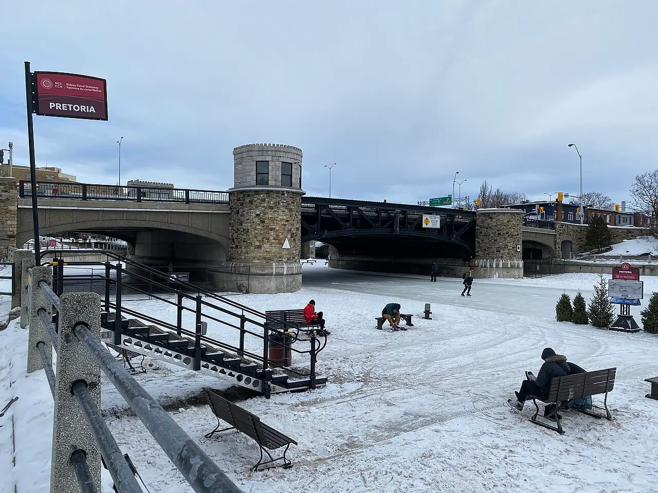 Skaters and benches on the frozen Rideau Canal Skateway beside the stone Pretoria Bridge in Ottawa