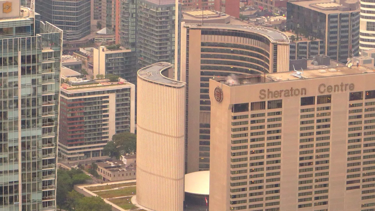 An aerial view over downtown Toronto with the curved towers of City Hall and surrounding office buildings, seen from the CN Tower