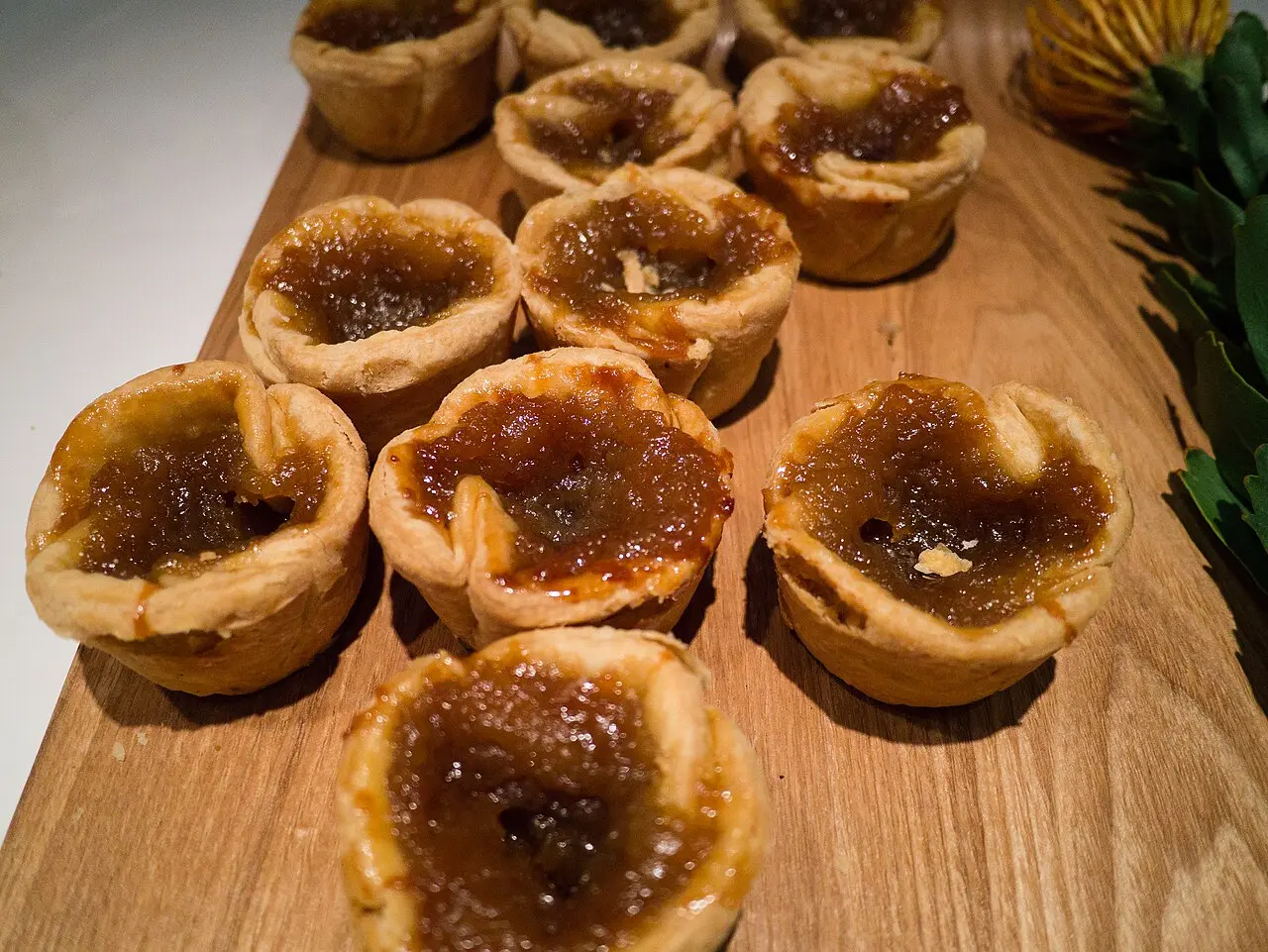 Several butter tarts with glossy dark filling in flaky pastry shells on a wooden board