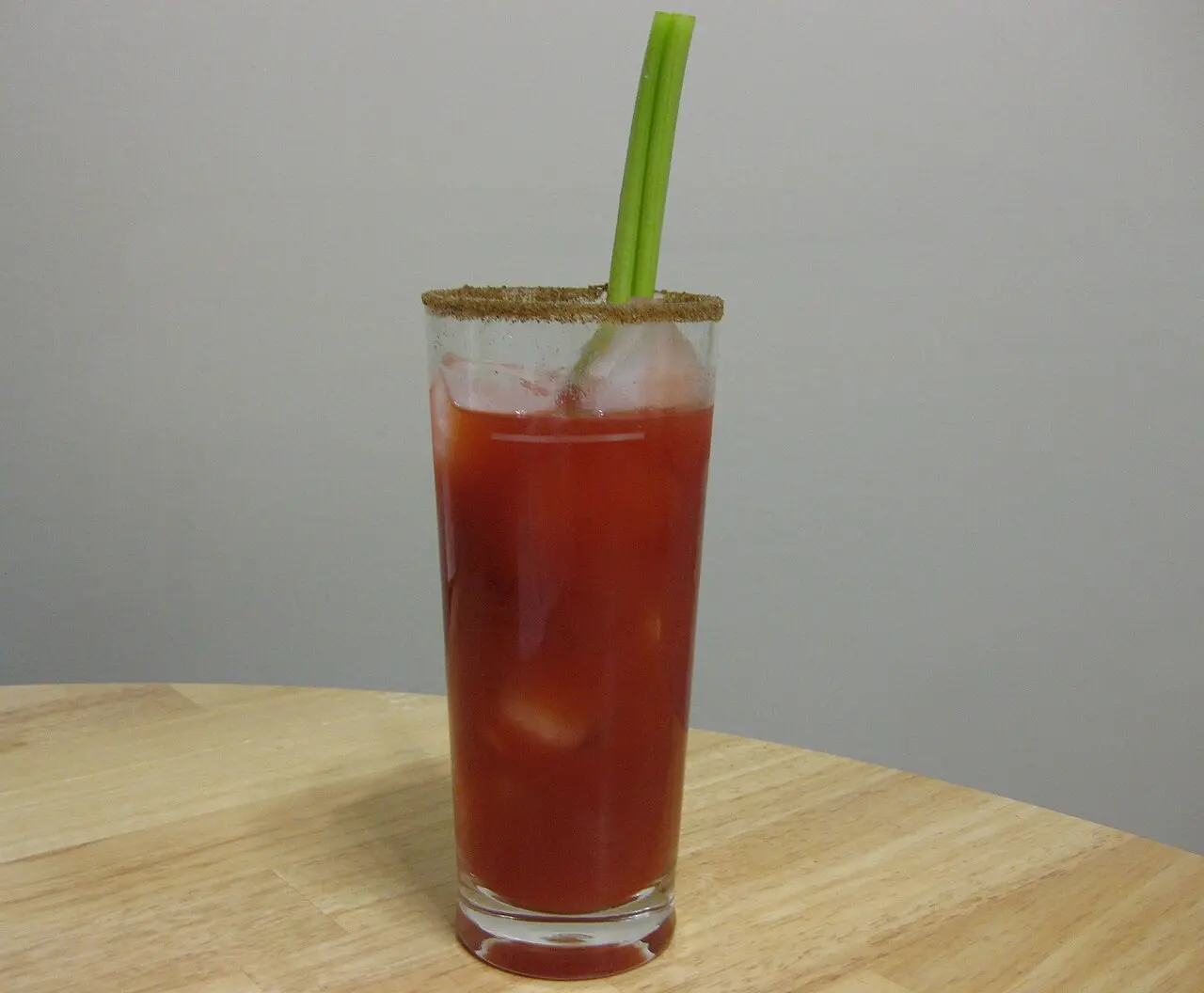 A Caesar cocktail in a tall glass with a celery-salt rim, ice and a celery stick