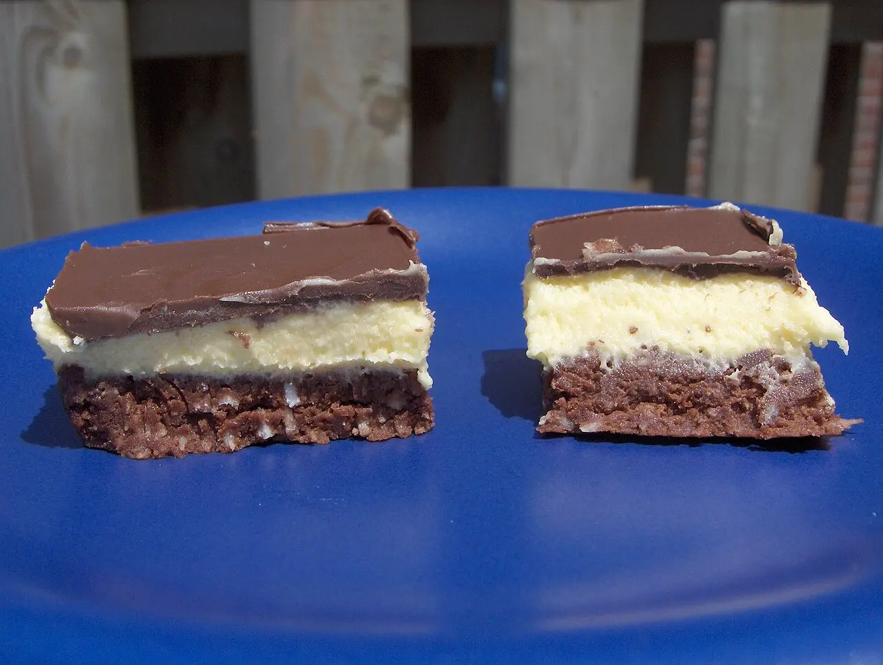 Two Nanaimo bars on a blue plate, showing the three layers of crumb, custard and chocolate