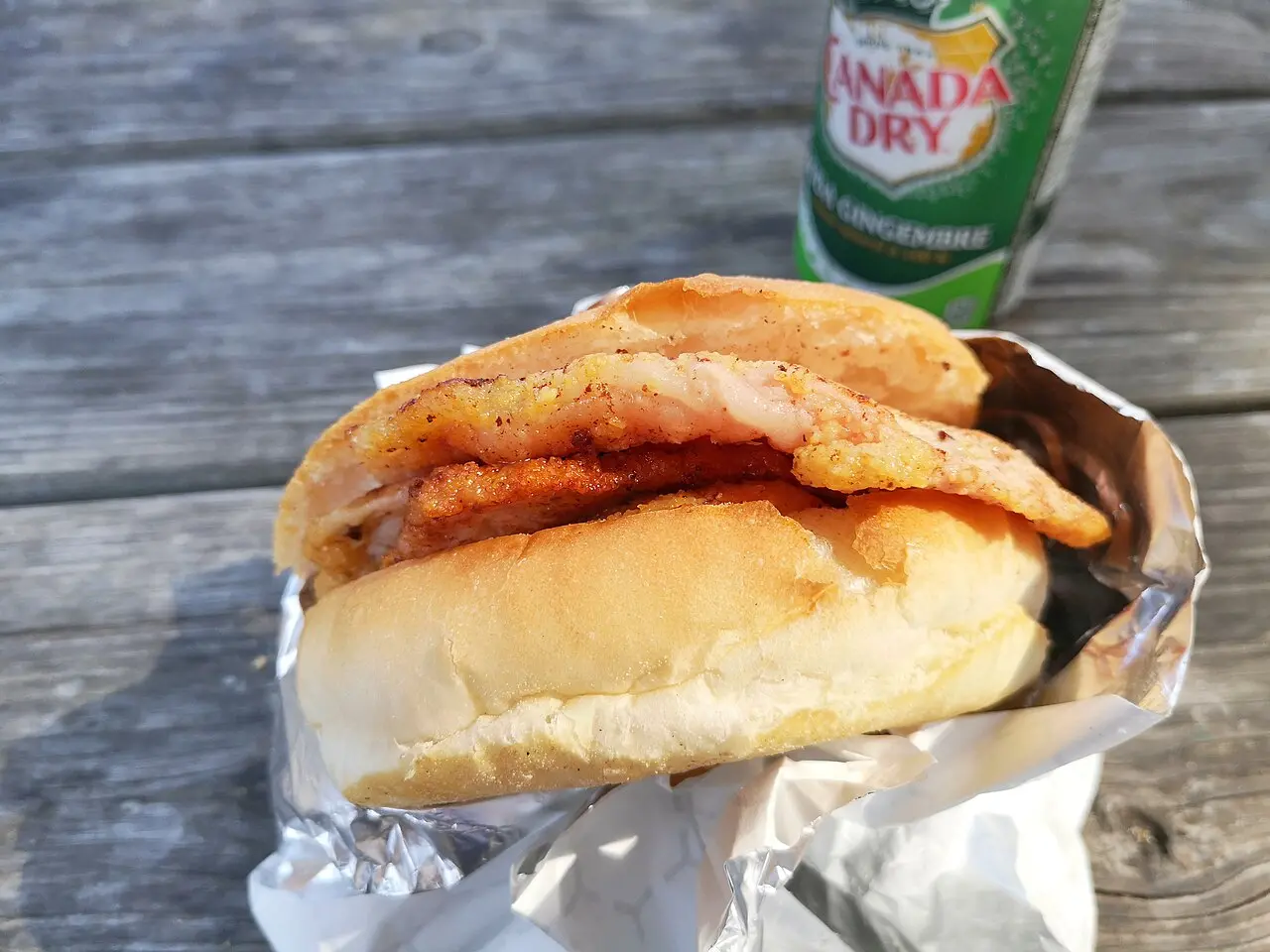 A peameal bacon sandwich on a soft bun, thick cornmeal-crusted pork visible in cross-section