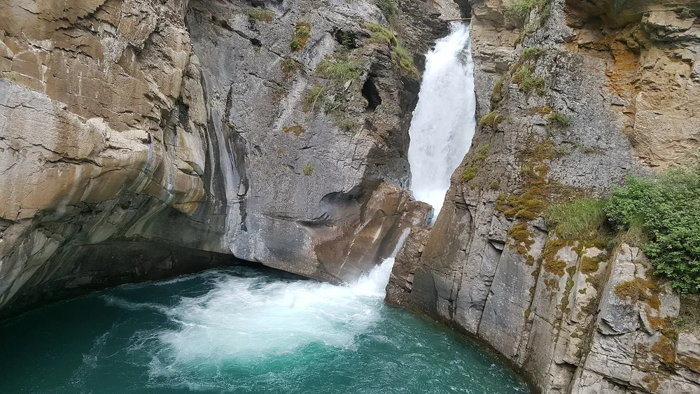 A steel walkway fixed to the sheer rock wall of Johnston Canyon above the fast green creek