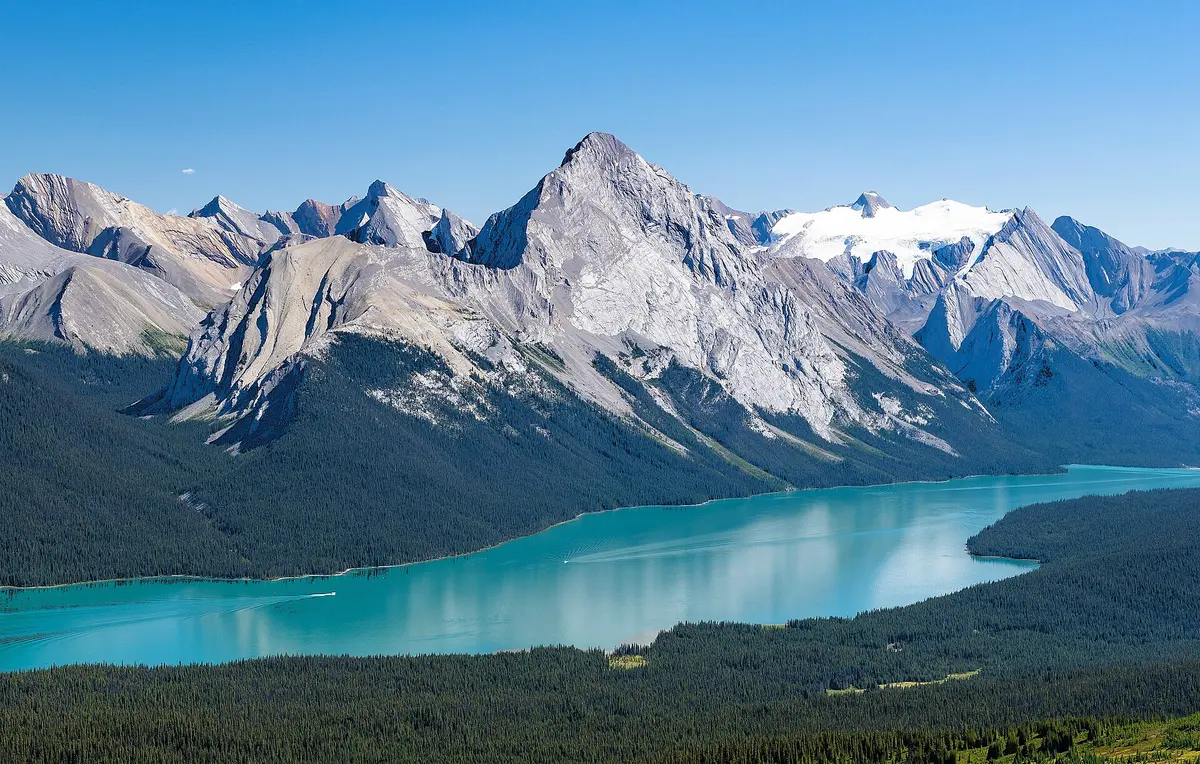 The blue water of Maligne Lake ringed by snow-streaked peaks under a clouded sky
