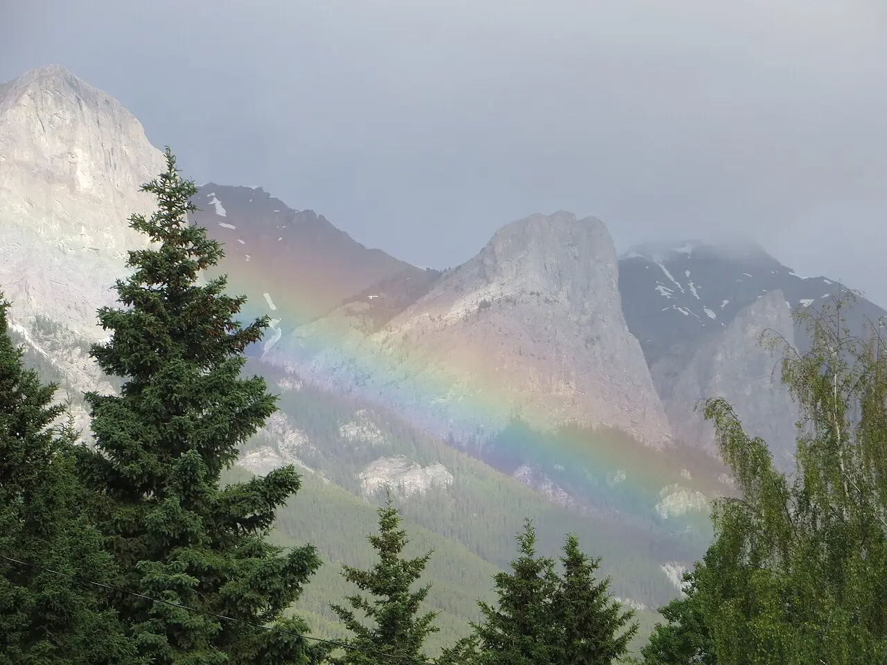 Rainbow over Canmore rooftops with dark storm light on the surrounding peaks