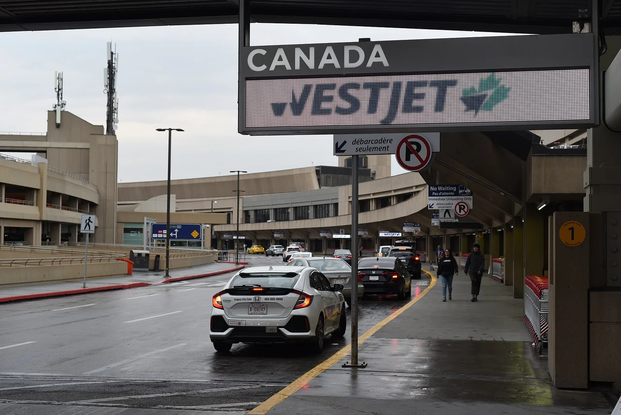 The wet Departures-level roadway at Calgary International Airport with a white taxi, an overhead WestJet sign and the terminal canopy running off to the right