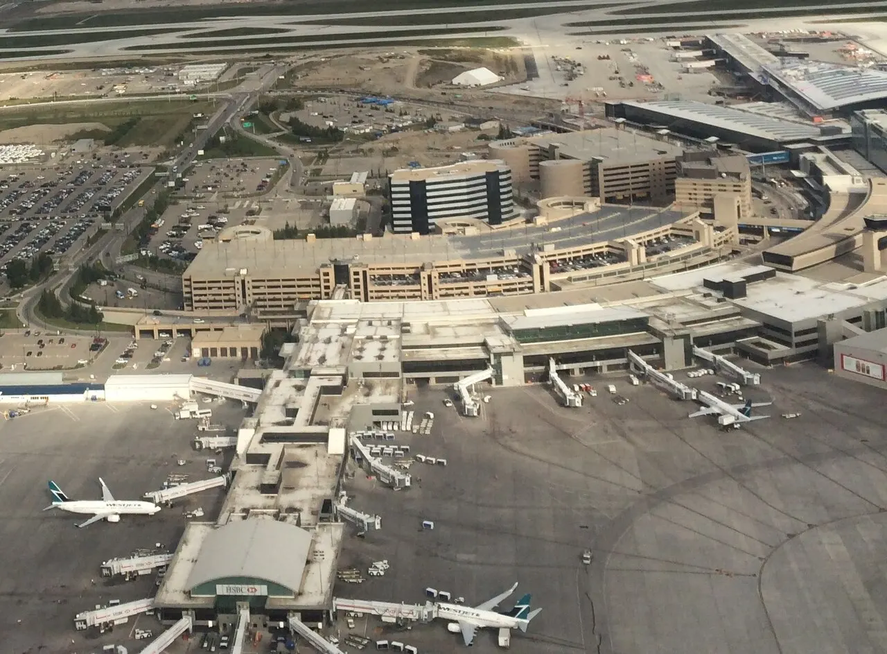 Aerial view of the Domestic Terminal at Calgary International Airport with a multi-storey parkade beside the curb roadway and a construction site at the upper right