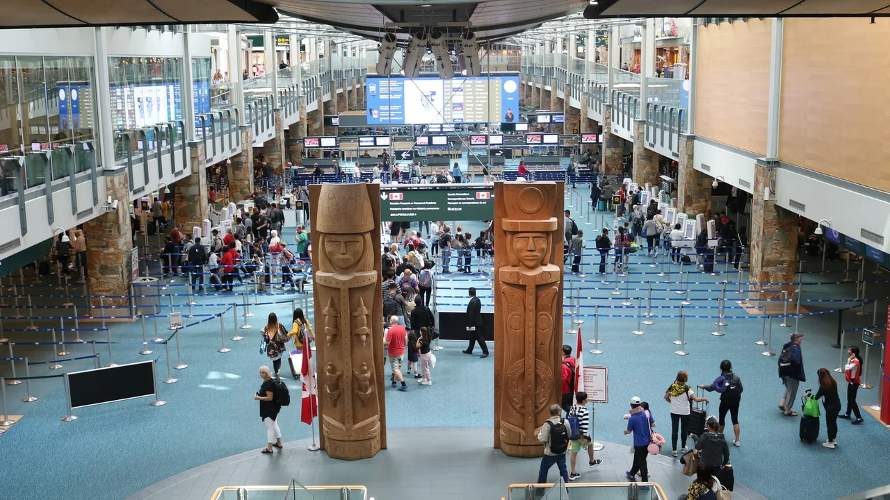 The international arrivals hall at Vancouver International Airport with two carved wooden figures standing in front of the queue barriers