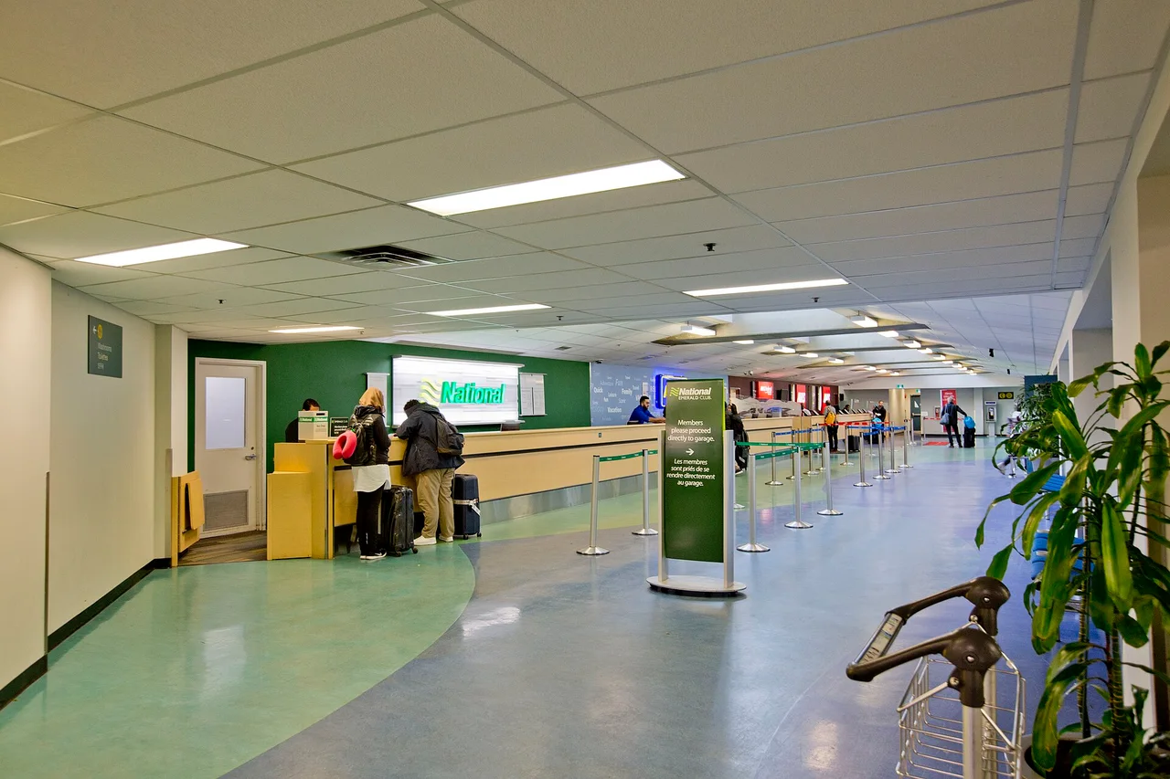 A long rental counter hall at Vancouver International Airport with queue barriers, a counter in use and travellers with suitcases
