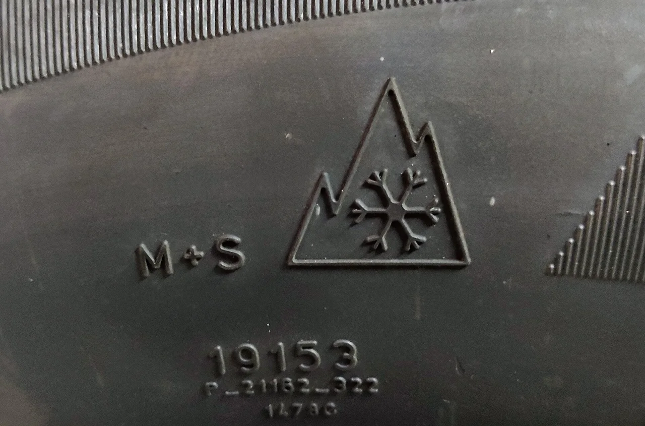 Close-up of a tire sidewall moulded with the letters M+S and the three-peak mountain snowflake symbol