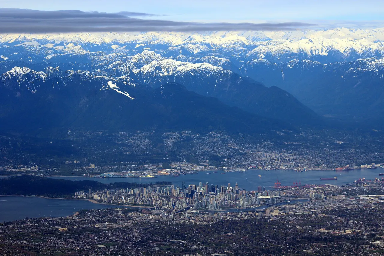Aerial view of downtown Vancouver on its peninsula with Burrard Inlet and the snow-capped Coast Mountains behind
