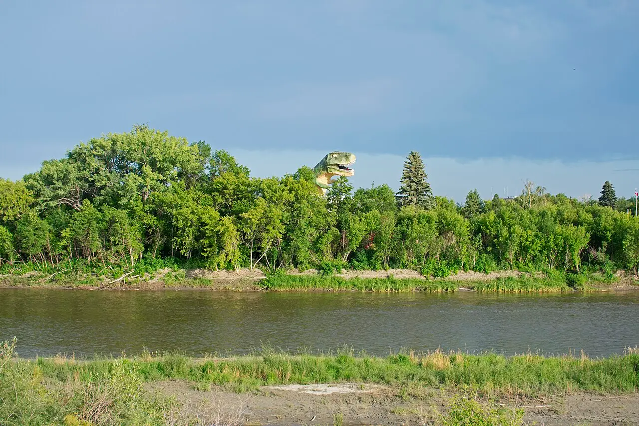 The head of the World's Largest Dinosaur statue rising above trees along the Red Deer River in Drumheller