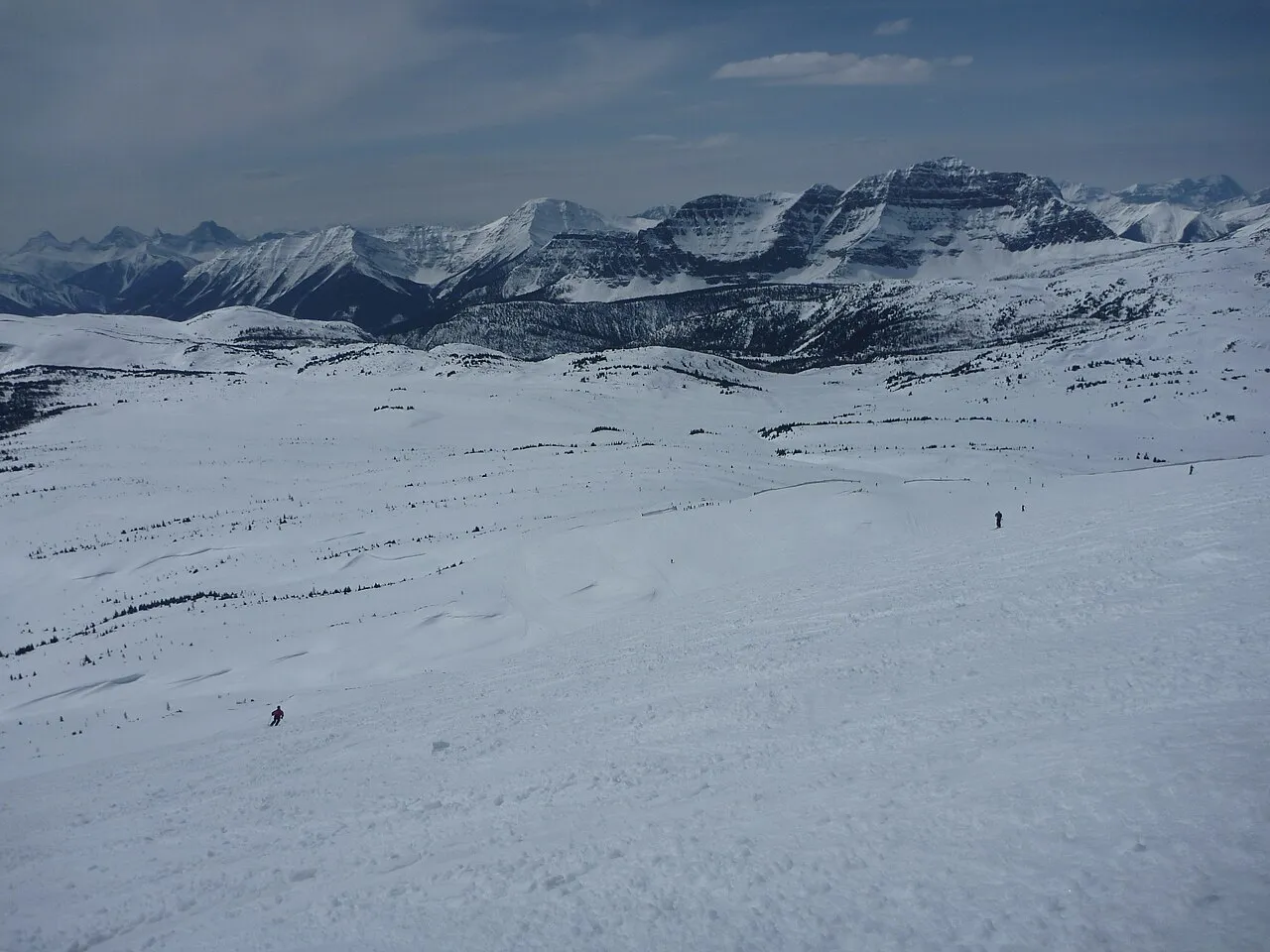 Skiers on a sunny spring day at Banff Sunshine with alpine ridges behind