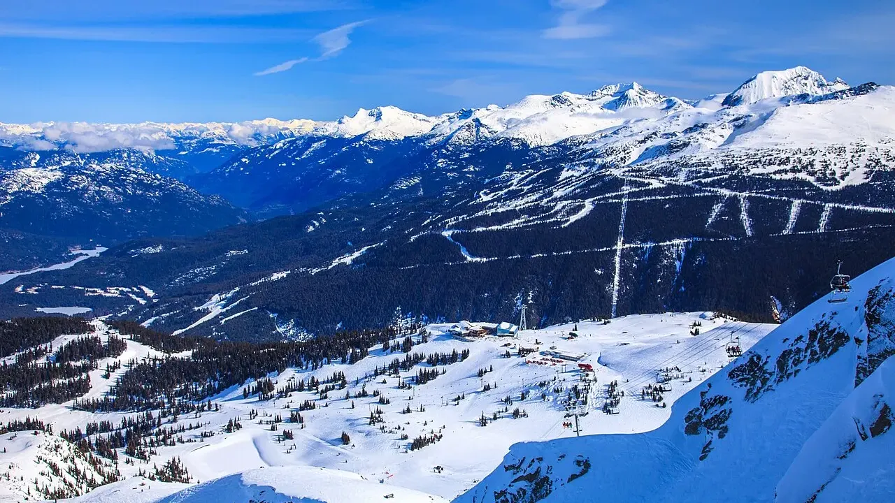 Alpine terrain and lifts above Whistler Blackcomb seen from the Roundhouse area, groomed runs cut through the forest with Blackcomb Mountain behind