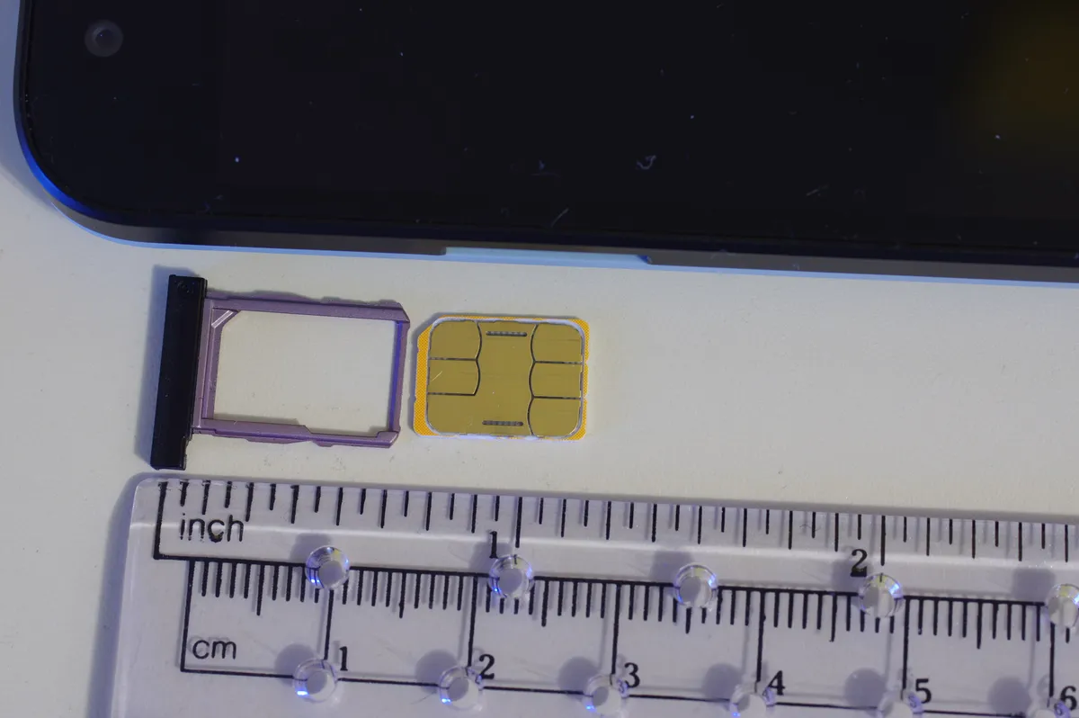 A nano SIM card resting on its ejected tray beside a smartphone