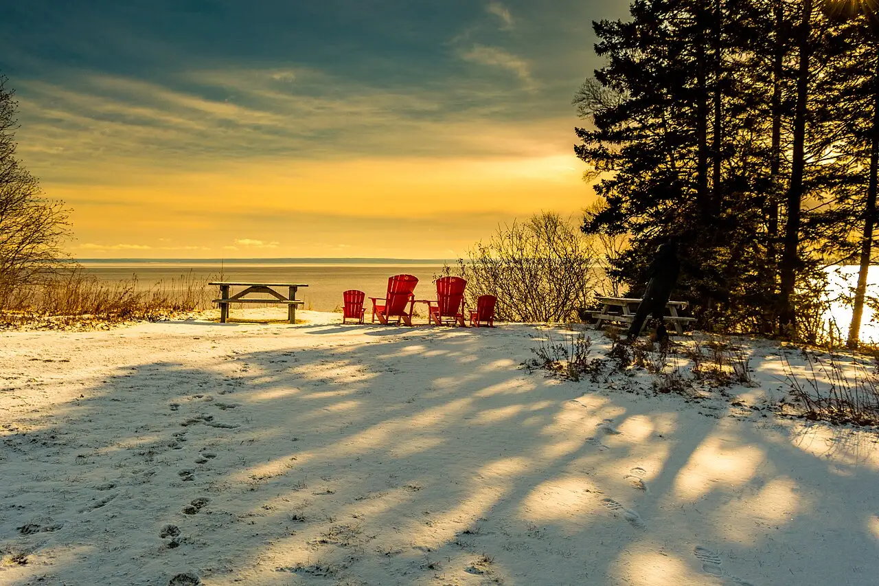 Red Muskoka chairs on a snowy overlook above the Bay of Fundy at sunset in Fundy National Park