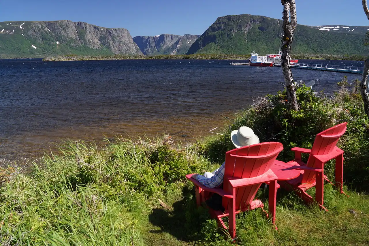 Two red Parks Canada chairs facing the cliffs and water of Western Brook Pond