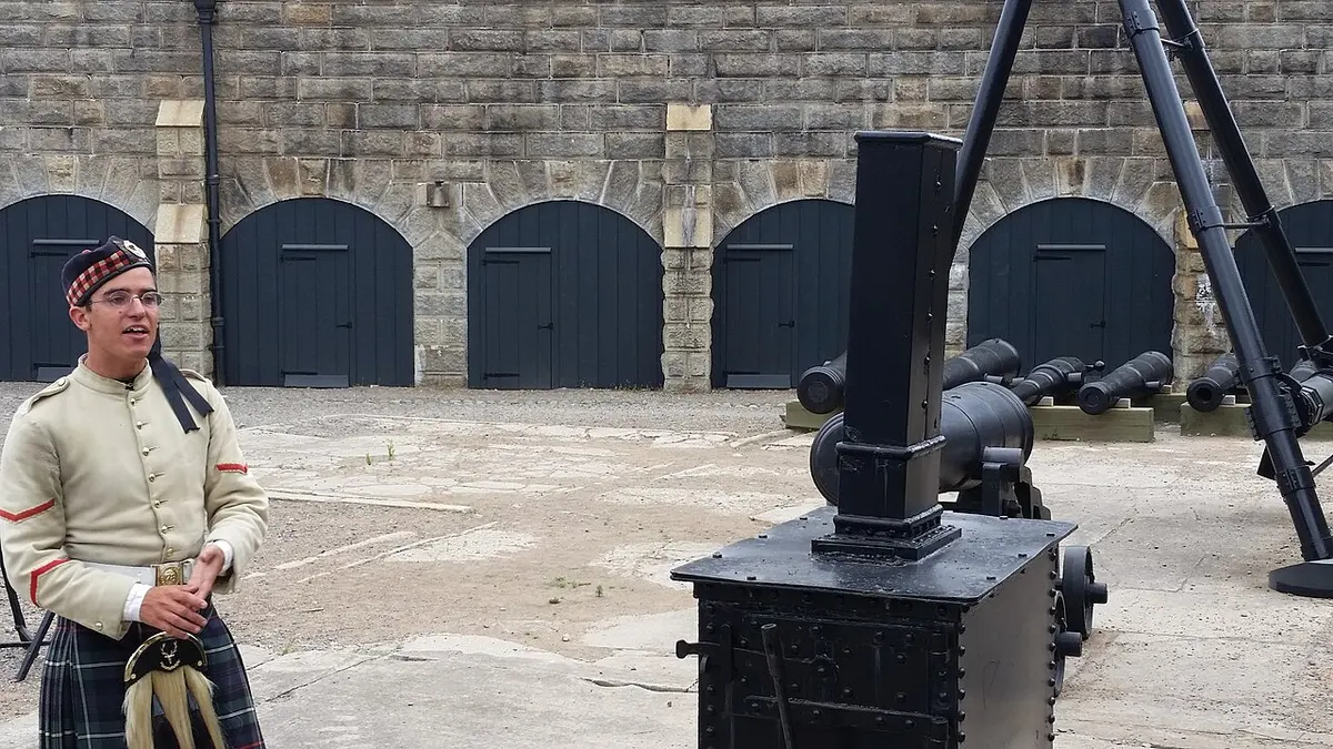 A re-enactor in 78th Highlanders uniform and kilt standing by cannons in the stone courtyard of Halifax Citadel