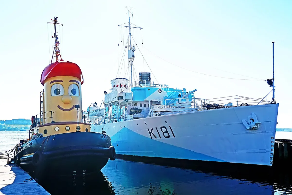 The smiling Theodore Too tugboat moored beside the grey and blue corvette HMCS Sackville on the Halifax waterfront