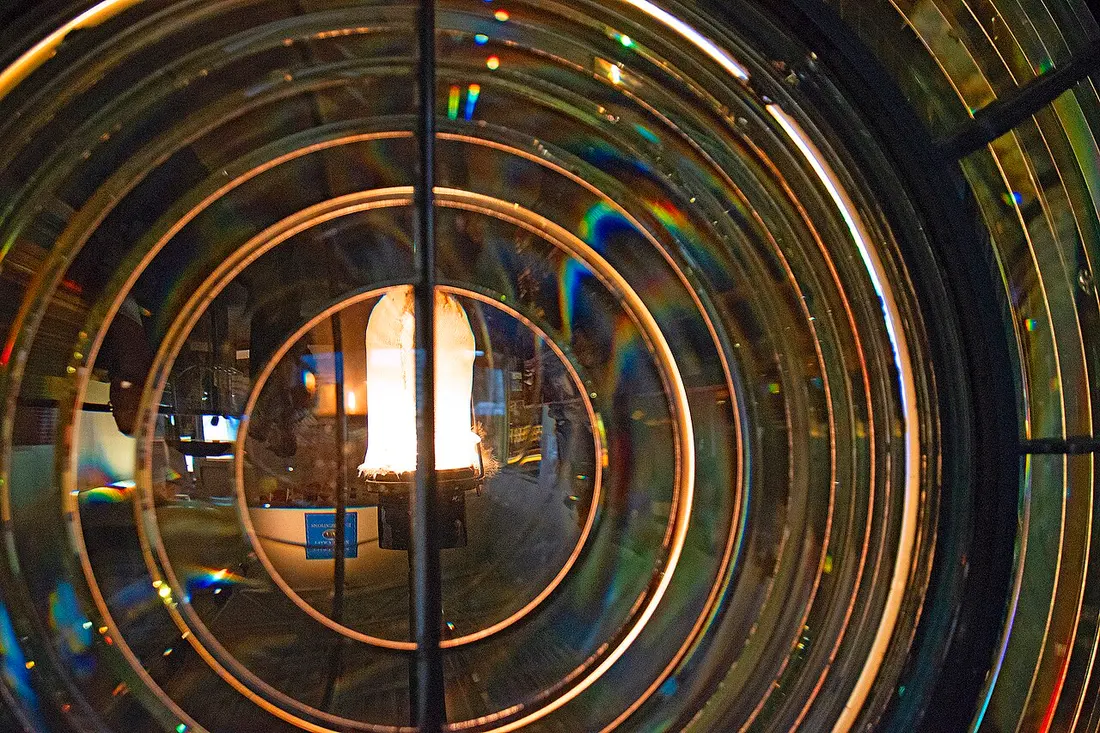Looking through the concentric glass rings of a lighthouse Fresnel lens with a lamp glowing at its centre in the Maritime Museum