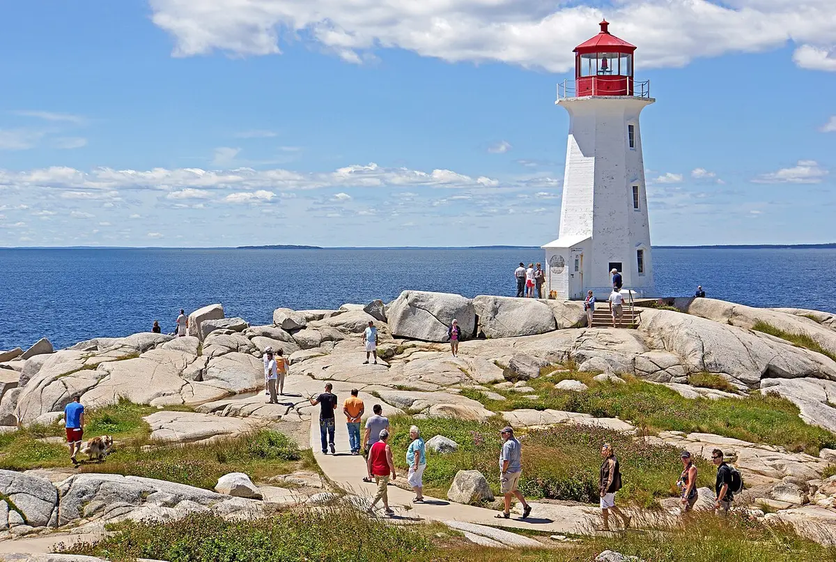 Peggy's Point Lighthouse on granite with crowds of visitors walking the rocks on a bright summer day
