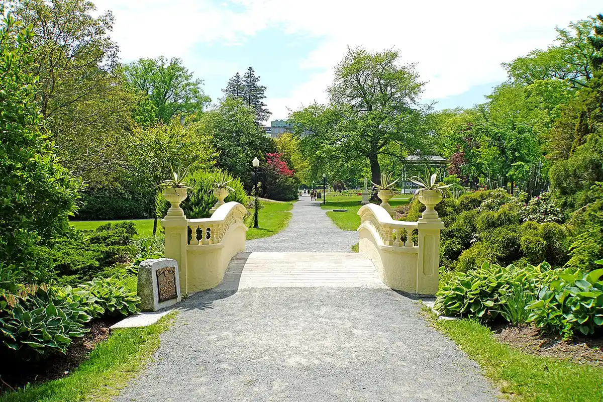 An ornamental white bridge with urn planters over a path in the lush green Halifax Public Gardens
