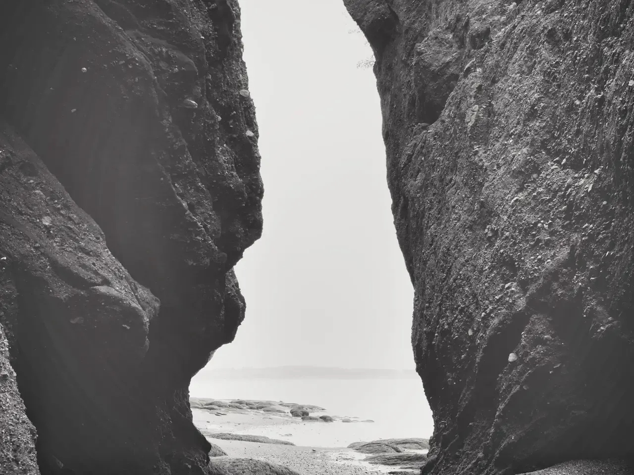 Black-and-white view through a cleft between two rock walls toward the water at Hopewell Rocks