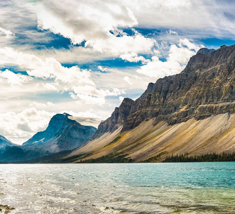 Bow Lake with grey scree slopes and a jagged peak rising straight from the far shore under tall clouds