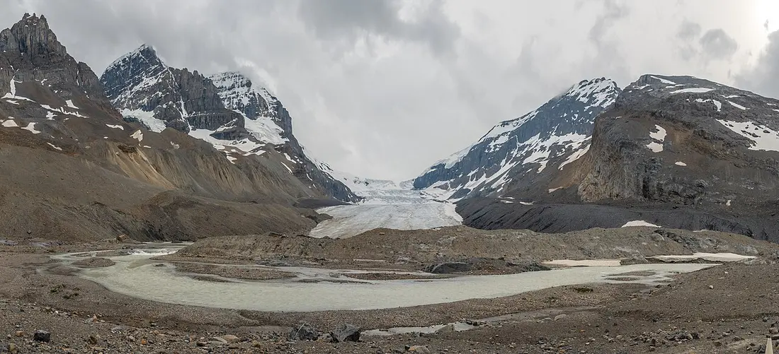 The Athabasca Glacier tongue seen from the grey moraine flats below, with meltwater channels in the foreground